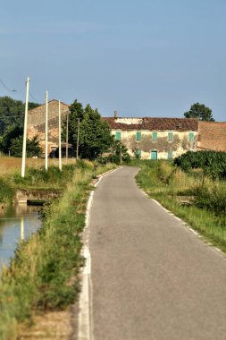 Tarlalı köy yolu ve yaz sonunda günbatımında terk edilmiş bir malikane.