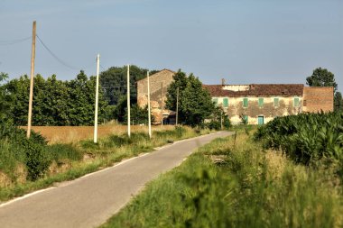 Tarlalı köy yolu ve yaz sonunda günbatımında terk edilmiş bir malikane.