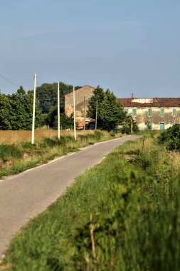 Tarlalı köy yolu ve yaz sonunda günbatımında terk edilmiş bir malikane.