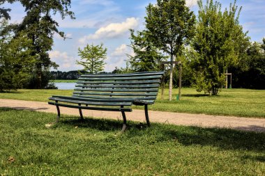Açık bir yaz gününde, bir yolun kenarında, nehrin yanındaki parkta bir bankta.