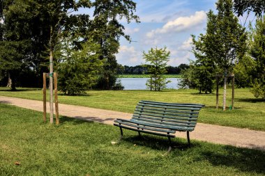 Açık bir yaz gününde, bir yolun kenarında, nehrin yanındaki parkta bir bankta.