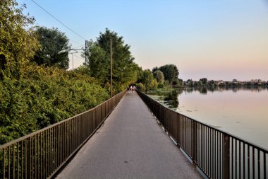Gün batımında bir koruluğa giden bir gölde gezinen insanlarla dolu bir geçit.