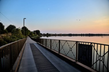 Gün batımında bir koruluğa giden bir gölde gezinen insanlarla dolu bir geçit.