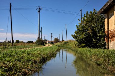 Terk edilmiş kır evi, temiz bir günde toprak bir yolun ve bir dere kenarındaki.