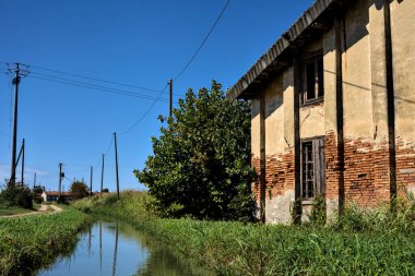 Terk edilmiş kır evi, temiz bir günde toprak bir yolun ve bir dere kenarındaki.