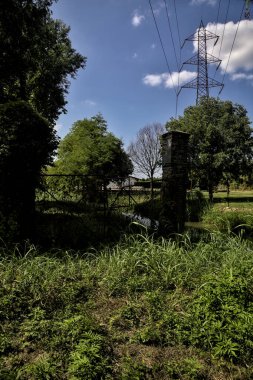 İtalya 'nın kırsal kesimlerinde terk edilmiş bir kapı tarafından engellenmiş bir su deresinin kıyısındaki bir korulukta yol.