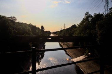 Gün batımında, açık bir günde, kırsal kesimdeki bir köprüde korkuluklu ve yolun bir parçası olan saptırma kanalı.