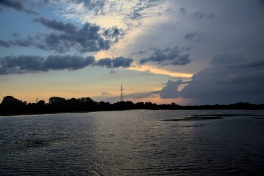 Gün batımında nehir kenarındaki bir parkın silüeti.