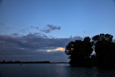 Alacakaranlıkta kıyıdaki koruluktan uzak bir nehirde kayık.