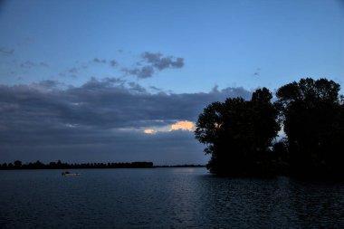 Alacakaranlıkta kıyıdaki koruluktan uzak bir nehirde kayık.