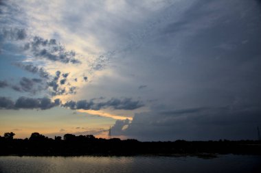 Gün batımında nehir kenarındaki bir parkın silüeti.