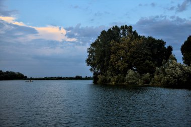 Alacakaranlıkta kıyıdaki koruluktan uzak bir nehirde kayık.