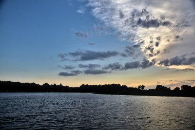 Gün batımında nehir kenarındaki bir parkın silüeti.