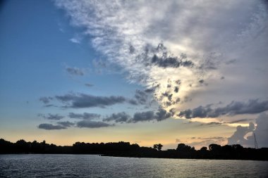 Gün batımında nehir kenarındaki bir parkın silüeti.