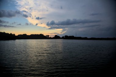 Gün batımında nehir kenarındaki bir parkın silüeti.