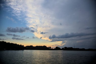 Gün batımında nehir kenarındaki bir parkın silüeti.