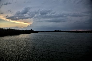 Gün batımında nehir kenarındaki bir parkın silüeti.