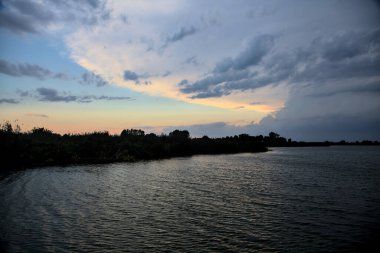 Gün batımında nehir kenarındaki bir parkın silüeti.