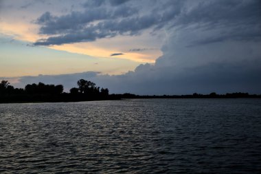 Gün batımında nehir kenarındaki bir parkın silüeti.