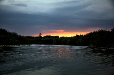 Yağmur yağmadan önce İtalya kırsalında bir nehrin üzerinde gün batımı