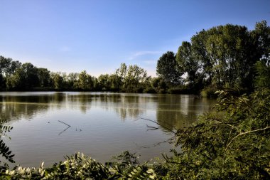 Gün batımında İtalya kırsalındaki bir parkta ağaçlarla çevrili bir nehrin körfezi.