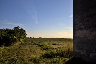 Gün batımında bir kır evi ve ağaçlarla dolu çıplak bir arazi.