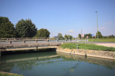 Road bridge over a diversionary channel with a trail next to it on a sunny day in the italian countryside