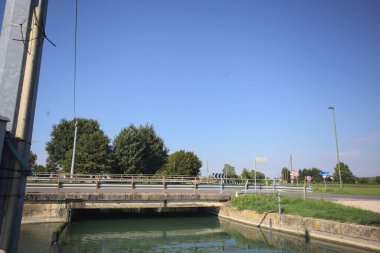 Road bridge over a diversionary channel with a trail next to it on a sunny day in the italian countryside