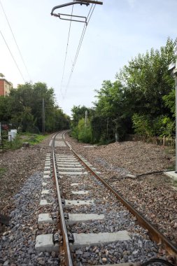 Railroad track passing through a patch of trees between buildings in an italian town on a cloudy day