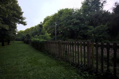 Railroad passing through a park in an italian town at sunset seen from its edge behind a fence