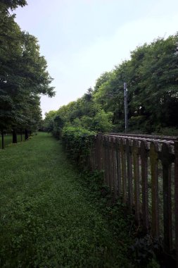 Railroad passing through a park in an italian town at sunset seen from its edge behind a fence