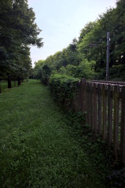Railroad passing through a park in an italian town at sunset seen from its edge behind a fence