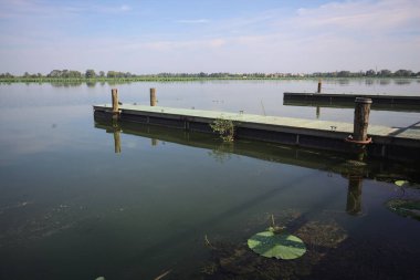 Pier with mooring poles on a lake with the sky casted in the water on a sunny day