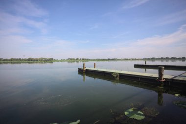 Pier with mooring poles on a lake with the sky casted in the water on a sunny day