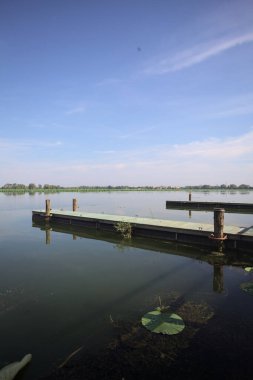 Pier with mooring poles on a lake with the sky casted in the water on a sunny day
