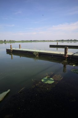Pier with mooring poles on a lake with the sky casted in the water on a sunny day