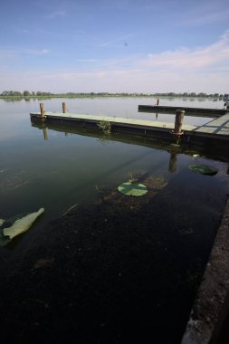 Pier with mooring poles on a lake with the sky casted in the water on a sunny day