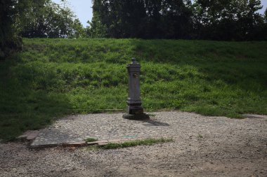 Fountain by the edge of a trail next to an embankment in a park