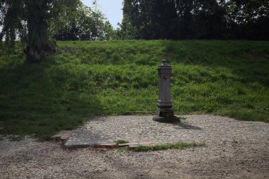 Fountain by the edge of a trail next to an embankment in a park