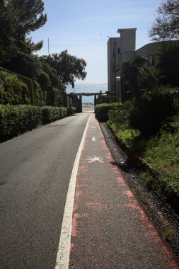 Descending road in a park by the seaside with a gate at the end of it