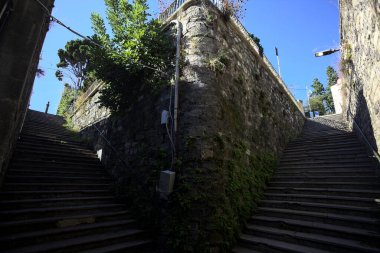 Stone staircases partially in the shade on a sunny day with a few plants on the walls in an italian town