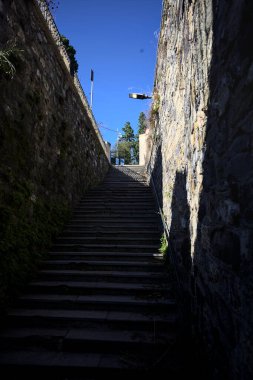 Stone staircases partially in the shade on a sunny day with a few plants on the walls in an italian town