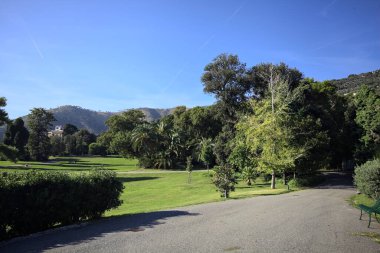 Park with trimmed lawns and trees on a sunny day with a mountain ridge in the background