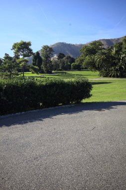 Park with trimmed lawns and trees on a sunny day with a mountain ridge in the background
