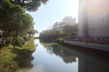 Deniz kıyısındaki bir italyan kasabasında bir korulukla suya atılan binaların arasından geçen bir nehir.