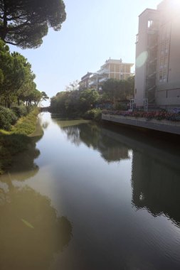 Deniz kıyısındaki bir italyan kasabasında bir korulukla suya atılan binaların arasından geçen bir nehir.