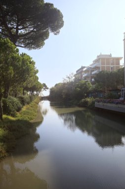 Deniz kıyısındaki bir italyan kasabasında bir korulukla suya atılan binaların arasından geçen bir nehir.