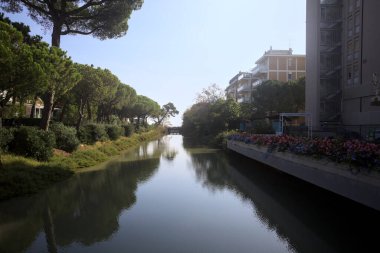 Deniz kıyısındaki bir italyan kasabasında bir korulukla suya atılan binaların arasından geçen bir nehir.