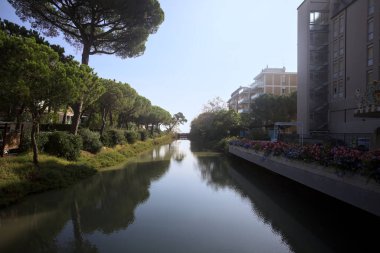 Deniz kıyısındaki bir italyan kasabasında bir korulukla suya atılan binaların arasından geçen bir nehir.