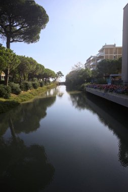 Deniz kıyısındaki bir italyan kasabasında bir korulukla suya atılan binaların arasından geçen bir nehir.